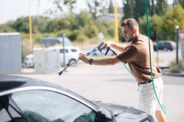Otomobil yıkamada yüksek basınçlı su kullanan genç bir adam. Yüksek kalite fotoğraf