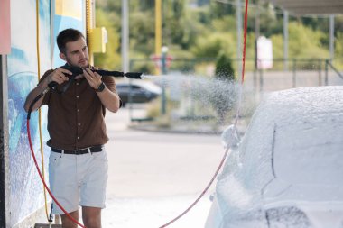 Cleaning car using active foam. Handsome man washing his luxury car on self car-washing. High quality photo clipart