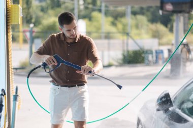 Otomobil yıkamada yüksek basınçlı su kullanan genç bir adam. Yüksek kalite fotoğraf