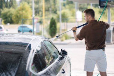Otomobil yıkamada yüksek basınçlı su kullanan genç bir adam. Yüksek kalite fotoğraf