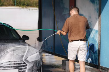 Cleaning car using active foam. Handsome man washing his luxury car on self car-washing. High quality photo clipart