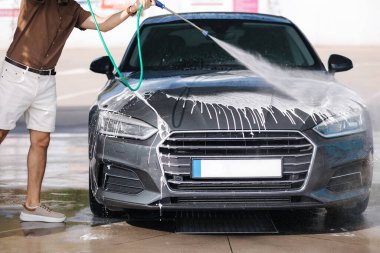 Araba yıkama. Yüksek basınçlı su kullanarak arabayı temizlemek. Lüks arabasını dışarıda yıkayan bir adamın orta seçimi. Yakın plan. Yüksek kalite fotoğraf