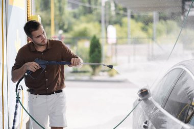 Arabasını jet spreyiyle temizleyen genç bir adamın yan görüntüsü. self servis araba yıkama. Yüksek kalite fotoğraf