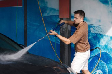 Arabasını jet spreyiyle temizleyen genç bir adamın yan görüntüsü. self servis araba yıkama. Yüksek kalite fotoğraf