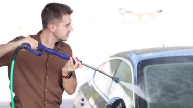 Otomobil yıkamada yüksek basınçlı su kullanan genç bir adam. Yüksek kalite 4k görüntü