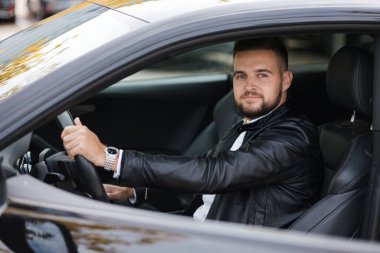 Başarı devrede. Arabada otururken deri ceketli yakışıklı bir genç. Yüksek kalite fotoğraf