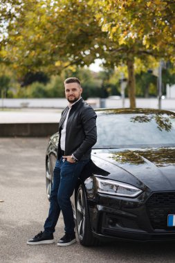 Yakışıklı sakallı adam lüks arabasının yanında duruyor. Deri ceketli şık bir erkek. Yüksek kalite fotoğraf