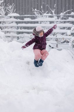 Arka bahçedeki kar tepesinde zıplayan sevimli küçük kız. Saf beyaz kar onu çevreledi. Yüksek kalite fotoğraf