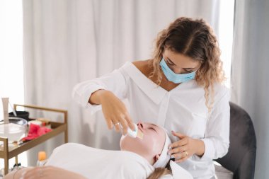 Koruyucu maske takan güzellik uzmanı bir müşteriye detaylı bir cilt bakımı uygular. Temizlik ve bakımı vurgular. Yüksek kalite fotoğraf