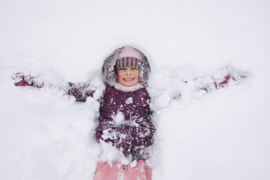 Kışlık giysiler içindeki küçük bir kız, karlı bir kış gününün büyüsünü yakalarken derin karlarla çevriliyken neşeyle gülümsüyor. Yüksek kalite fotoğraf