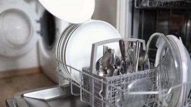 İnsan eliyle dolu bir bulaşık makinesinden temiz tabakları çıkartırken çekilmiş yan görüntü. Açık çamaşır makinesinin arka planı. Yüksek kalite 4k görüntü