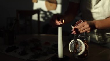 Bir kadın kibritle mum yakar ve sıcak bir ev ortamı yaratır. Güneş ışığı odaya akar, sıcaklık ve sükunet ekler. Yüksek kalite 4k görüntü