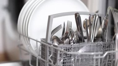 Kadın eli, bulaşık makinesine temiz çatal bıçak koydu. Açık çamaşır makinesinin arka planı. Yüksek kalite 4k görüntü