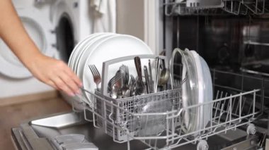 Kadın eli dolu bir bulaşık makinesinden temiz çatal bıçak takımını çıkarıyor. Açık çamaşır makinesinin arka planı. Yüksek kalite 4k görüntü