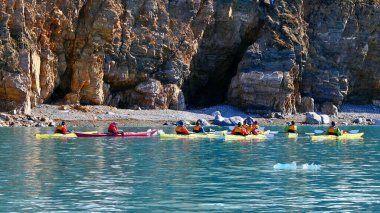 Svalbard, Norveç - 29 Mayıs 2023: Parlak renkli kanolar içindeki bir grup meçhul gezgin açık güneşli bir günde Krossfjorden 'in kayalık kıyılarını keşfediyorlar