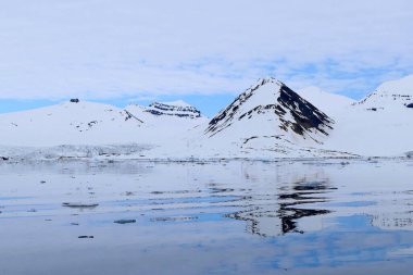 Manzaralı kutup manzarasının soğuk renkleri karla kaplı kayalık dağların ve dalgalanan sulardaki mavi gökyüzünün yansımaları. Svalbard takımadaları, Norveç