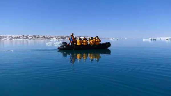 Svalbard, Norveç 29 Mayıs 2023: Açık ve güneşsiz bir günde Krossfjorden sularının sakin yüzeyinde şişme bir botla gezen turistler grubu