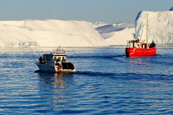 Ilulissat, Grönland 9 Temmuz 2019: Büyük bir buzullu güzel manzara, küçük bir motorlu tekne ve bilinmeyen turistlerle dolu kırmızı bir balıkçı teknesi Icefjord, UNESCO Dünya Mirası Bölgesi 'nde gün batımını izliyor 