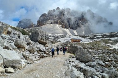 Dolomitler, İtalya - 16 Haziran 2024: Laghi-dei-Piani gölünün kıyısındaki tanınmayan genç çiftin Güney Tyrol 'daki Tre Cime Doğa Koruma Alanındaki güzel manzaraya hayran kalmaları