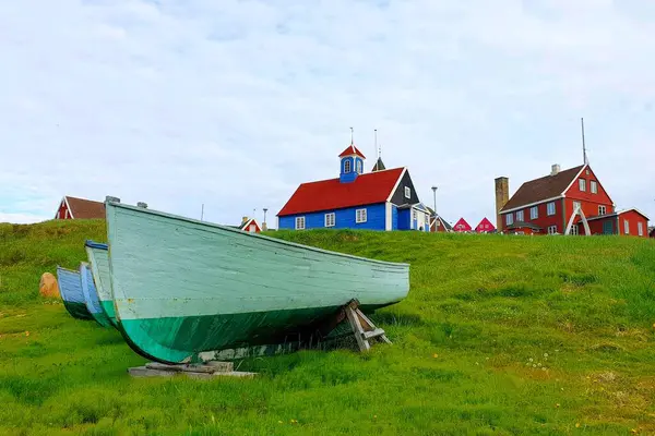 Grönland 'da bir yaz günü bulutlu bir gökyüzüne karşı parlak boyanmış geleneksel evler ve renkli balıkçı tekneleriyle Sisimiut balıkçı kasabasının manzarası.