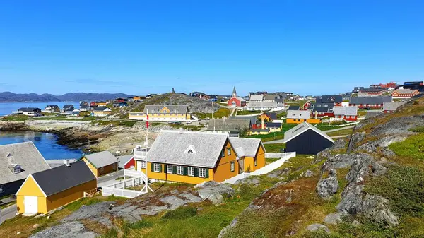 Uçurumun tepesinden şehrin tarihi merkezine kadar parlak renkli evler, uzak bir kırmızı kilise ve açık güneşli bir yaz gününde, Grönland 'ın başkenti Nuuk' ta fiyordun mavi suları.