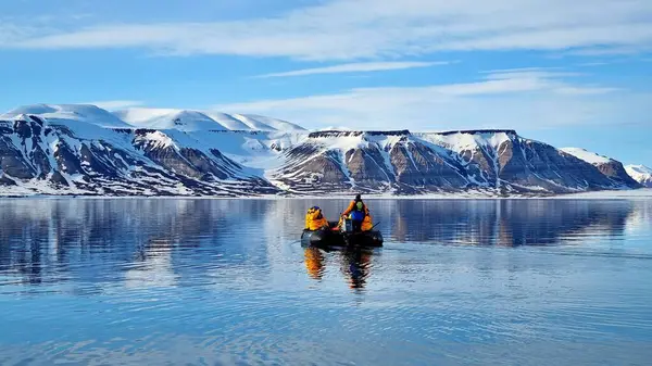 Norveç, Svalbard takımadalarında güneşli bir yaz gününde, bir botta, karla kaplı dağlarda, bilinmeyen insanlarla dolu manzaralı bir deniz manzarası.