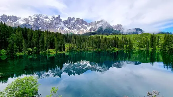 Dağ gölü Lago di Carezza ile nefes kesen manzara ve İtalya 'nın Güney Tyrol Dolomitleri' ndeki karlı dağların yansımaları.