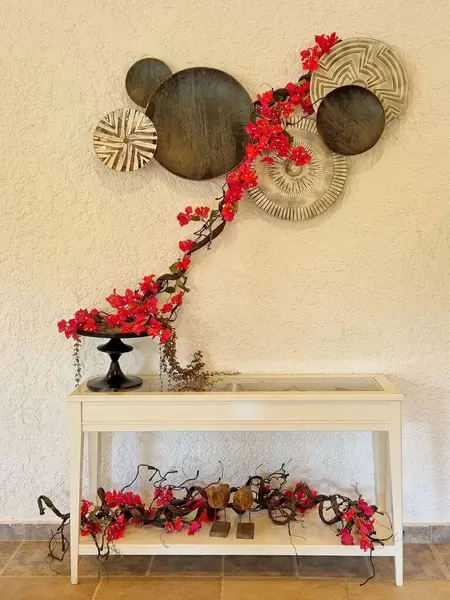 Evin iç dekorasyonu Japon tarzında, farklı boyutlarda ahşap diskler ve konfigürasyonlar, bougainvillea dalları ve duvarın renginde iki katlı küçük bir masadan oluşmaktadır.