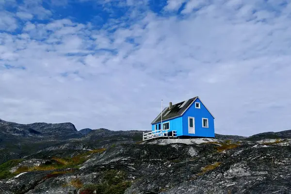 Grönland 'ın kıyısında beyaz kabarık bulutları olan güzel mavi gökyüzünün zemininde, kayalık bir tepede yalnız küçük bir ev.