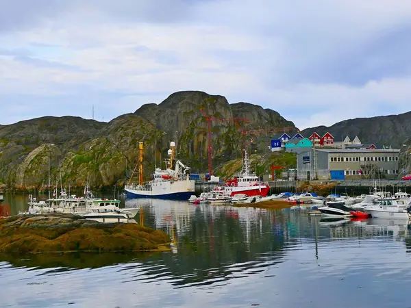 Danimarka 'nın Batı Grönland kentindeki Maniitsoq liman kasabasında yaz sabahı bulutlu bir gökyüzüne karşı balıkçı tekneleri ve kayalık deniz kıyısındaki renkli Eskimo evleri olan resimli deniz manzarası.