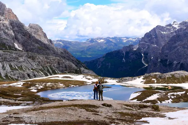 Dolomitler, İtalya - 16 Haziran 2024: Laghi-dei-Piani gölünün kıyısındaki tanınmayan genç çiftin Güney Tyrol 'daki Tre Cime Doğa Koruma Alanındaki güzel manzaraya hayran kalmaları
