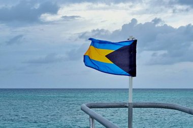 Bahamalar 'ın bayrağı, güzel Eleuthera adasındaki tatil köyündeki mavi denize karşı dalgalanıyor.