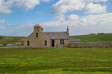 Geleneksel mimari tarzında taştan bir çiftlik evi. Büyük bir tarlanın ortasında. Uzak Orkney Adaları, İskoçya, İngiltere 'de yeşil çimenler var.