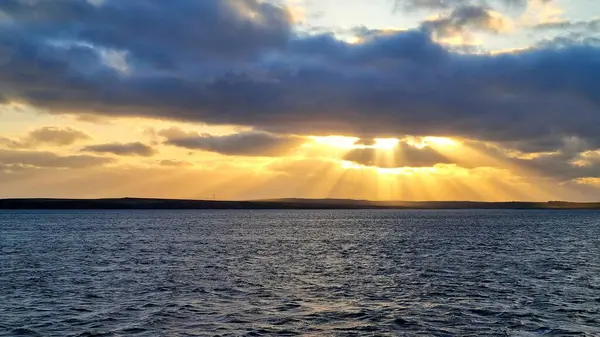 Batan güneşin altın ışınları bulutların karanlığına nüfuz eder ve Atlantik Okyanusu 'nun karanlık sularını aydınlatır. 
