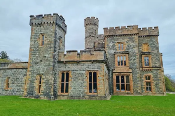 Bulutlu gökyüzüne karşı yeşil çimlerde antik neo-gotik Viktorya kalesi