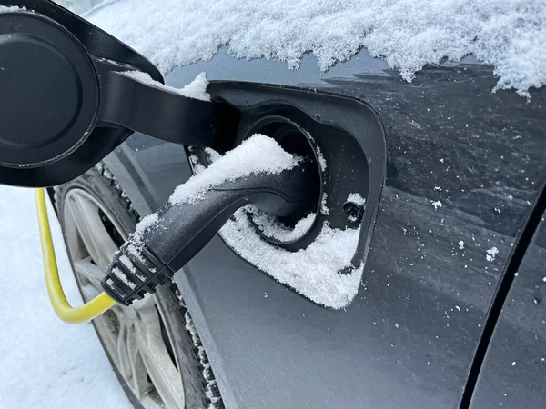Close up of charging electric car in the winter with snow outside. Concept of charging electric vehicle in cold weather. Photo taken in Sweden.