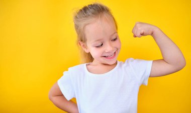 strong shiny school girl showing arm muscles isolated yellow color background successful training workout