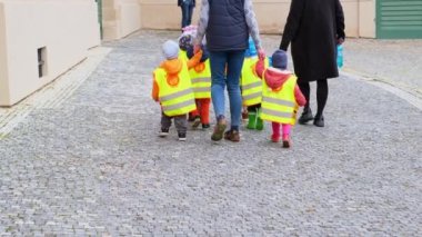 Bir grup küçük çocuk emniyet kemeri takmış çocuklarla çocuk yuvasında yürüyor.