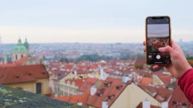 Turist kadın, şehrin akıllı telefonunun resmini çekti. Prag 'ın en üst panoramik şehrinin çatıları üzerinde..