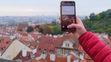 Turist kadın, şehrin akıllı telefonunun resmini çekti. Prag 'ın en üst panoramik şehrinin çatıları üzerinde..