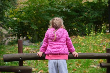Pembe ceketli küçük anaokulu kızı parkın sonbaharında gözlerini kaçırıyor. Yüksek kalite fotoğraf