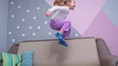 Playful Happy little girl dancing and having fun jumping in the room on the bed. High quality 4k footage