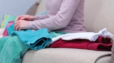 Mother woman sitting on sofa and folding the baby children clothes laundry. High quality 4k footage