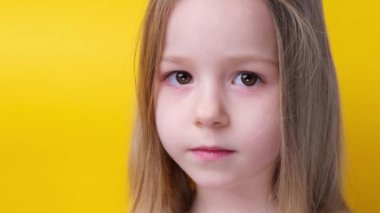 Close up smiling little girl before haircut Look at the camera scissors in hand yellow background. High quality 4k footage