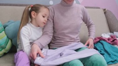 tired little girl assisting mother clothes folding laundry household cores . High quality 4k footage