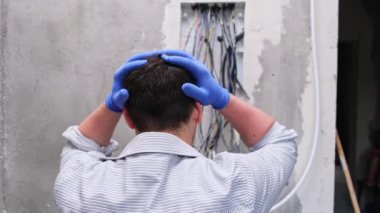 Genç elektrikçi ya da tamirci bağlantıları tamir ederken ya da kontrol ederken yoruldu. Erkek elektrikçi yeni bir elektrik kablosuna kablo ve kablo döşeme konusunda şaşkın.