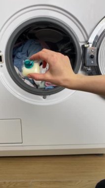 Kadın ellerini kapat. Çamaşır makinesinin içinde çamaşır deterjanı olan renkli jel deterjan kapsülünü kirli çamaşırlara koy. Yüksek kalite 4k görüntü