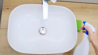 Üst düzey kadın evdeki banyoda temizlik yapıyor, lavabo ve musluğu sprey bez süngerle temizliyor mikrofiber sünger dezenfekte konseptiyle temizliyor. Yüksek kalite 4k görüntü