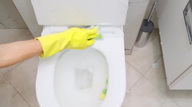 Evin süngerindeki tuvaleti yavaş çekimde temizleyen kadın sarı lastik eldiven giyen kadın temizlikçi temizleyici sprey köpüklü tuvalet kapağını dezenfektanla dezenfekte ediyor. 4k görüntü
