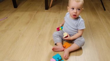 Bebek elma yer ve mutfakta oynar hafif bir zeminde oturur, küçük bir oyuncakla meşgul olur, oyuncu yaratıcılığı geliştirir. - Evet. Yüksek kalite 4k görüntü